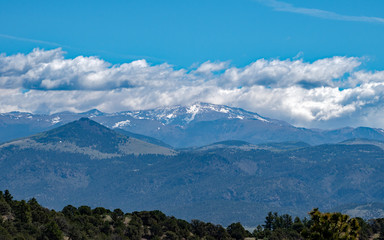 Pretty white clouds in the blue sky hover over the Colorado mountains on a hazy day making a pretty scene. Bokeh.