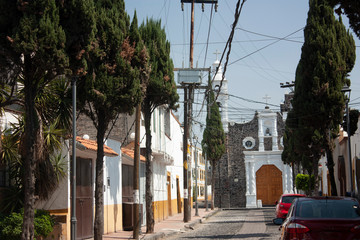 Stoned streets of Mexico City in a magical rustic town of the Assumption with the typical white walls painted with yellow in the background an 18th-century church is observed