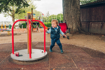 Funny toddler boy having fun on playground, rides toy car on merry-go-round