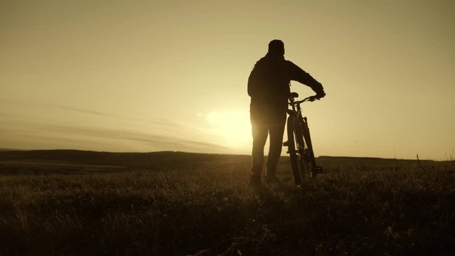 Silhouette of the mountain bicycle rider on the hill with bike at sunset. Sport, travel and active life concept.