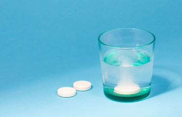 Dissolving an effervescent tablet in a glass of water at blue background with copy space