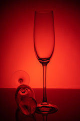 Two empty glasses of champagne with reflection, on a red and black background gradient background. Concept, party and club life. Magazine and commercial photo with place for text or design, festival