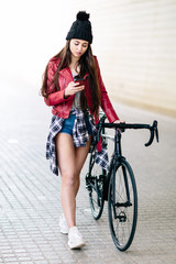 Fototapeta na wymiar Attractive young woman consults her smartphone while walking down the street with her bilicleta holding the handlebar