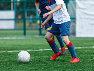 Boys in white and blue sportswear plays football on field, dribbles ball. Young soccer players with...
