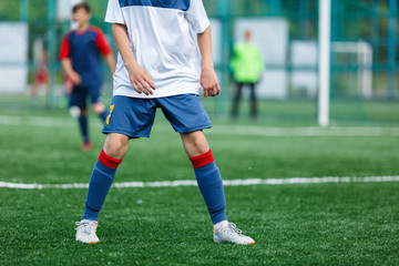 Boys in white and blue sportswear plays football on field, dribbles ball. Young soccer players with ball on green grass. Training, football, active lifestyle for kids concept