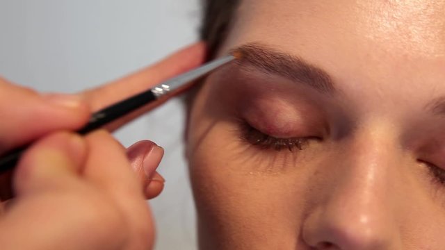 make up artist fills in a gorgeous girl's eyebrow. white background .
