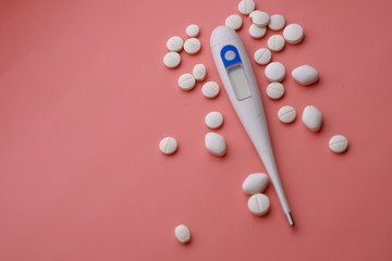close up of pills and thermometer on pink background 