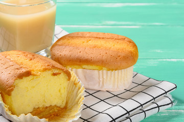 two cup cakes and one with some bites and cup of soy milk on back horizontal composition