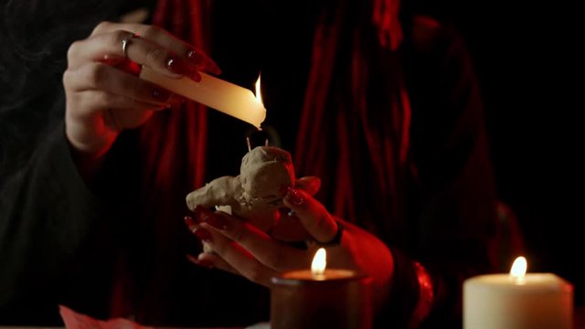Cropped view of witch with candle dripping wax on voodoo doll during occult ritual