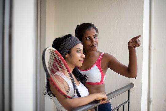 Indian black and white brunettes girls with a tennis bat enjoying themselves in sportswear on a balcony in a white background. Indian lifestyle