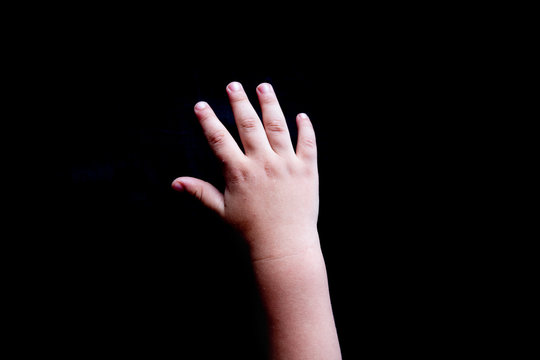 Open white baby hand with palm facing down on a black background