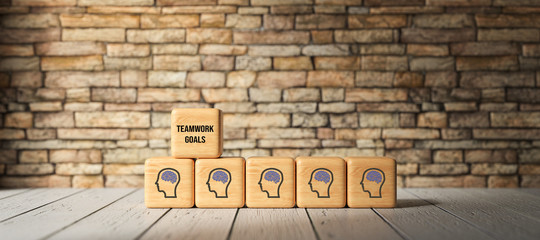Fototapeta na wymiar cubes with person-symbols and the message TEAMWORK GOALS in front of a brick wall on wooden floor