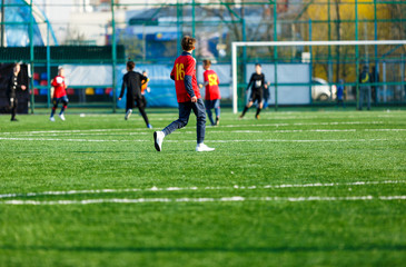 Boys in red and black sportswear plays football on field, dribbles ball. Young soccer players with ball on green grass. Training, football, active lifestyle for kids concept