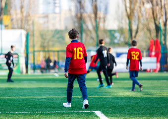 Boys in red and black sportswear plays football on field, dribbles ball. Young soccer players with ball on green grass. Training, football, active lifestyle for kids concept