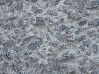 Uneven wall of large crushed stone of gray color in white stucco