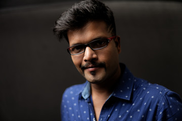 Portrait of a handsome and intelligent Indian brunette man wearing blue shirt with white stars sitting on a chair. Indian lifestyle and fashion portrait