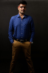 Portrait of a handsome and intelligent Indian brunette man wearing blue shirt with white stars  standing before a copy space black background. Indian lifestyle and fashion portrait