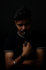 Close up portrait of a handsome and intelligent Indian brunette man wearing a solid black t shirt standing before a copy space black background holding a tobacco. Indian lifestyle and fashion portrait