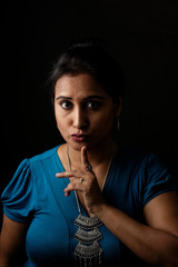 Close up face portrait of a beautiful Indian Bengali brunette woman in light and shadow before a black copy space background wearing a blue top. Indian lifestyle and fashion  portrait