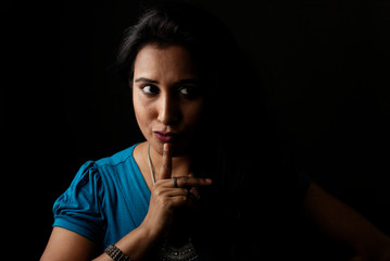Close up face portrait of a beautiful Indian Bengali brunette woman in light and shadow before a black copy space background wearing a blue top. Indian lifestyle and fashion  portrait