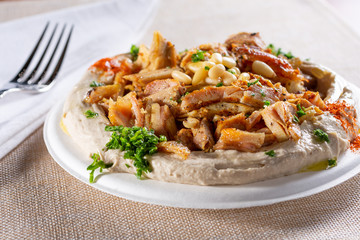 A view of a plate of chicken shawarma on top of hummus, in a restaurant or kitchen setting.