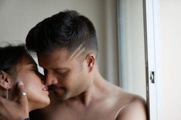 Indian Bengali beautiful brunette couple sharing intimate romantic moments standing in front of a window in white background. Indian lifestyle  and romantic couple