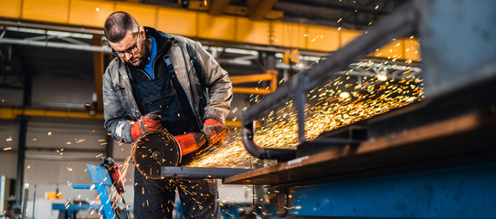 Factory worker cutting metal with grinder.