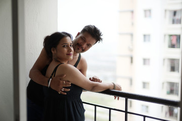 Portrait of a beautiful Indian Bengali brunette romantic couple wearing black  dresses enjoying rain while standing on the balcony. Indian lifestyle and fashion portrait