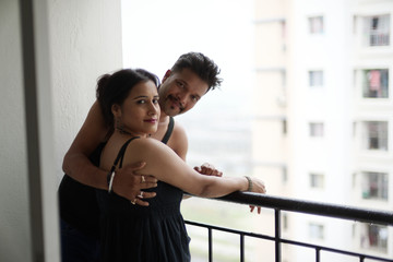 Portrait of a beautiful Indian Bengali brunette romantic couple wearing black  dresses enjoying rain while standing on the balcony. Indian lifestyle and fashion portrait