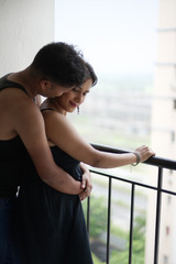 Portrait of a beautiful Indian Bengali brunette romantic couple wearing black  dresses enjoying rain while standing on the balcony. Indian lifestyle and fashion portrait
