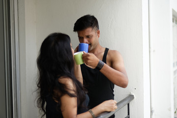 Indian Bengali beautiful brunette couple in black dress sharing intimate romantic moments while drinking tea/coffee standing on balcony in white background. Indian lifestyle  and romantic couple