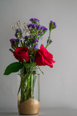 Obraz premium Red roses with purple flowers bouquet in a clear glass jar. Repurpose, from trash to treasure idea.