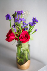 Red roses with purple flowers bouquet in a clear glass jar. Repurpose, from trash to treasure idea.