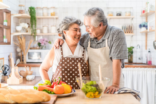 Couple senior Asian elder happy living in home kitchen. Grandfather cooking salad dish with grandmother with happiness and smile enjoy retirement life together. Older people relationship and activity.