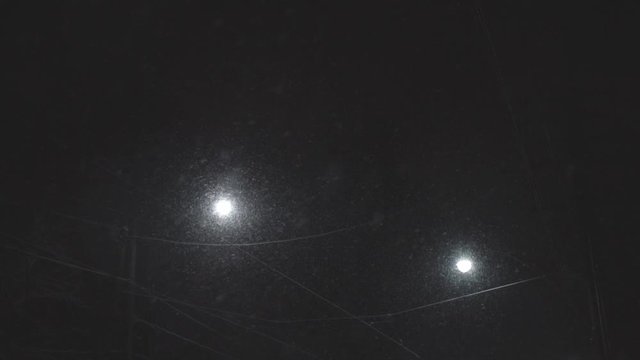 Snowflakes falling on a dark night with backlit of glowing streetlights - Pan upshot