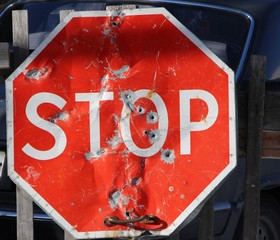 old cramped stop sign with round holes hanging on the fence