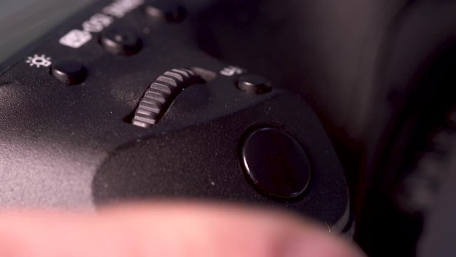 Close up/macro footage of a photographer's  finger pushing the button on a DSLR Camera and making adustments to settings before taking more photographs.