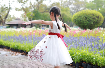 Little girl in white dress walking with flowers around in the garden. Rear view.