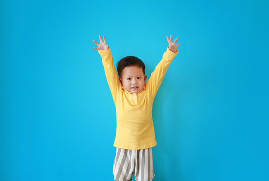 Portrait Of Happy Little Asian Baby Boy Expression Raise Hands Up And Looking Camera Isolated Over Blue Background.