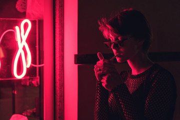 Fashion sexy tomboy hipster short hairstyle woman wear stylish glasses stand near neon street red...