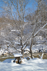 Snow-covered wooden table on the shore of a mountain river.