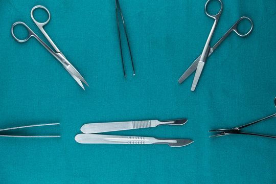 Top view of surgical instrument, stainless steel scalpel handle number 3 with blade number 10 and scalpel handle number 4 with blade number 24 and tweezers, scissors on surgical green drape fabric.