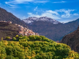 In the High Atlas mountains of Morocco, a Berber village is perched on a steep hillside, with snowcapped Jbel Toubkal, the tallest mountain in North Africa, in the background.