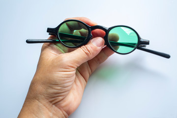 Woman's left hand holding black sunglasses on white background, Close up & Macro shot, Selective focus, Optical concept