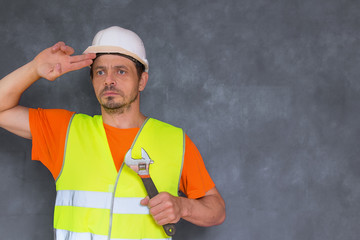 Locksmith - repairman in a white helmet and a yellow vest. A fitter with a determined face looks forward. In the hands of a large wrench. The repairman adjusts the helmet on his head. Handyman.