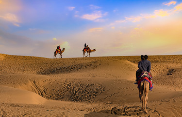 Tourist couple enjoy camel safari at the Thar desert Jaisalmer Rajasthan at sunset