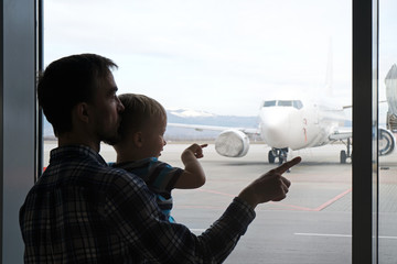 Silhouette of father and son looking and pointing by fingers at airplane through the window of airport terminal. Family journey, travel with child lifestyle. - Powered by Adobe