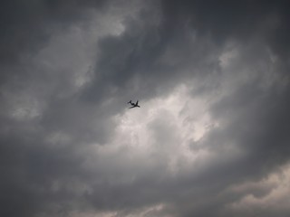 Naklejka na ściany i meble Airplane flying at a height on a background of thunderclouds at the black and white sky. Plane flying to a black cloudy sky before a thunderstorm. Airplane and thunder front. Dangerous flight. 