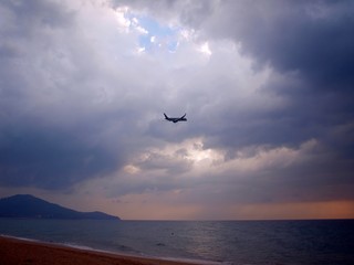 Fototapeta na wymiar Deserted beach and a plane in the sky flying under a thundercloud in a ray of light. Stormy landscape and a plane flying into the clearance between the clouds. Danger and risk. Dangerous piloting