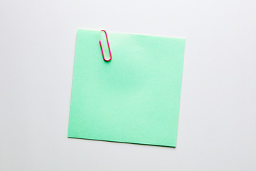Blank green note paper or notepad with a red paper clip on white background with copy space